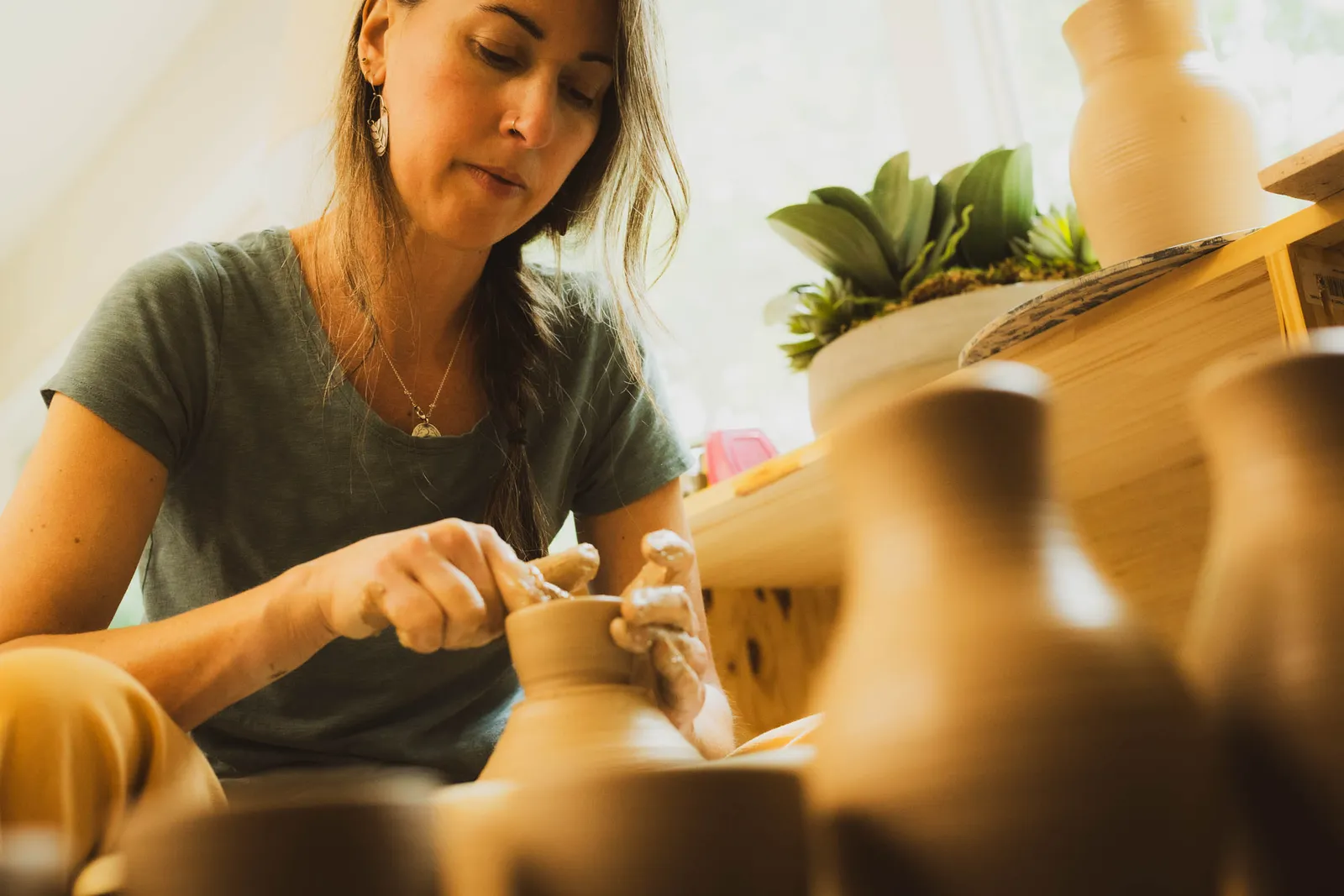 Karissa Masse shaping a small clay vessel by hand, with unglazed vases in the foreground.
