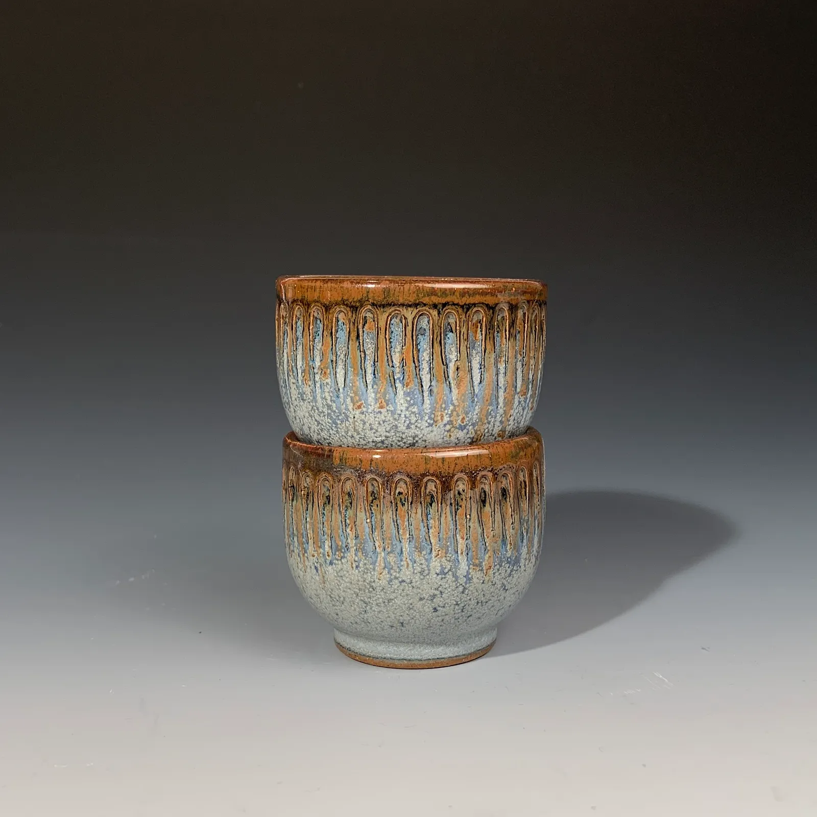 Two stacked Peacock cups in a blue and white speckled glaze with an orange-brown carved, drippy rim.
