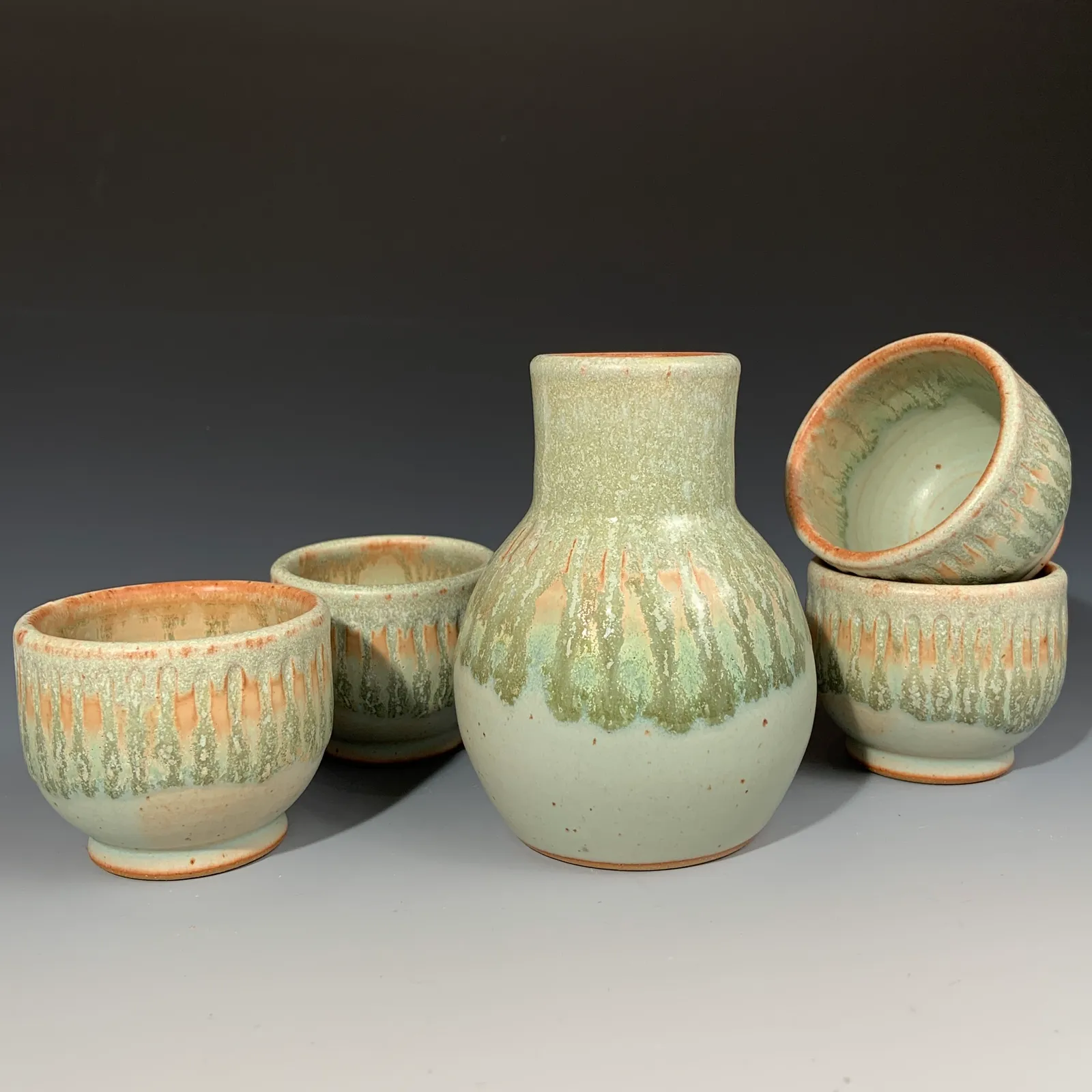 Willow bottle and four small cups in pale jade green glaze with warm orange drips.