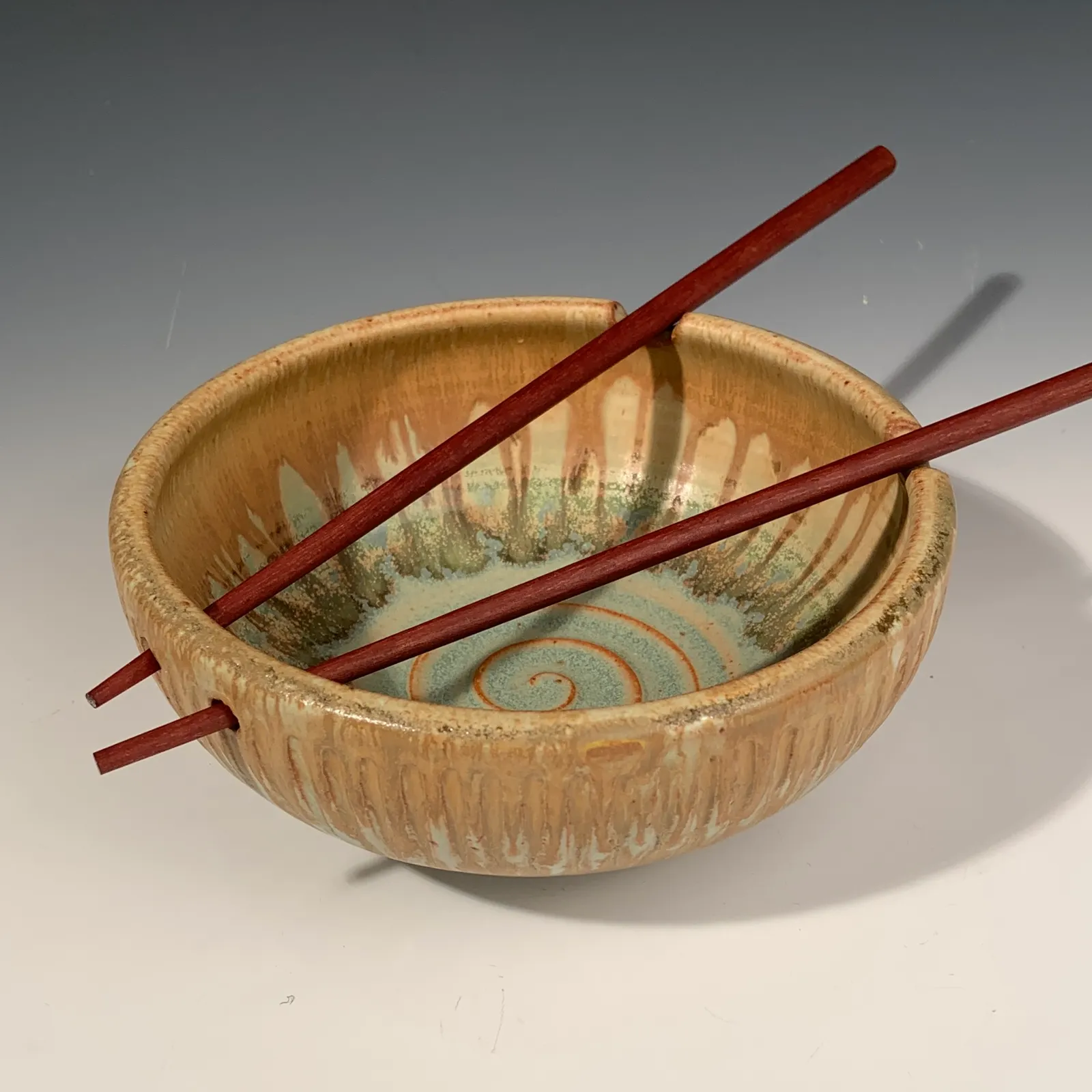 Willow bowl with a carved ochre exterior and spiral-glazed interior, with red wooden chopsticks resting in notches on the rim.