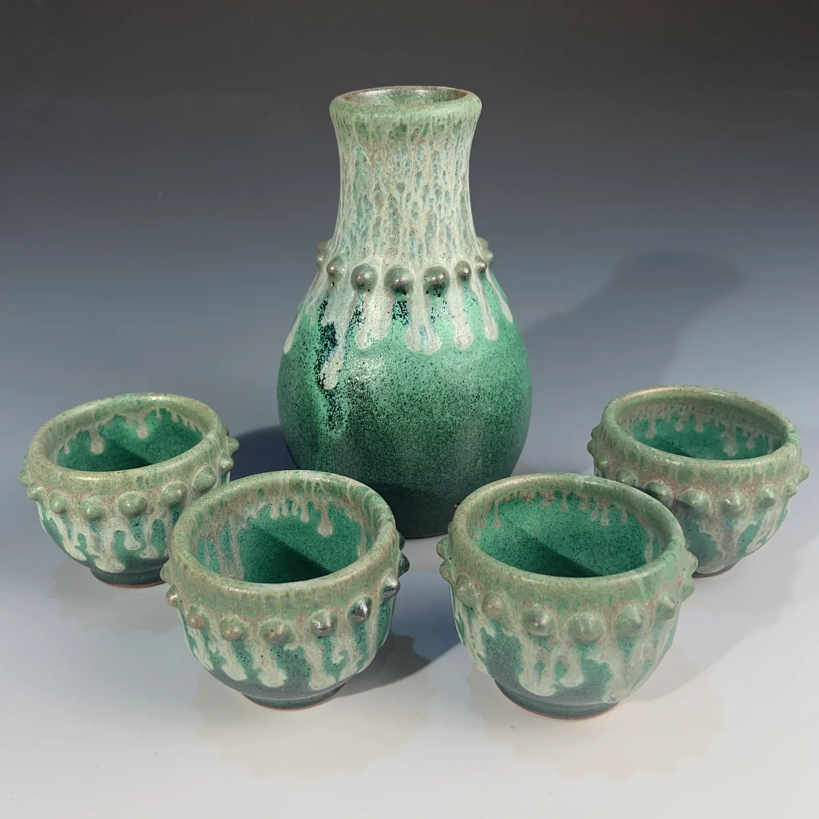 Juniper bottle and four small cups in green glaze with creamy white drips and beaded rims.