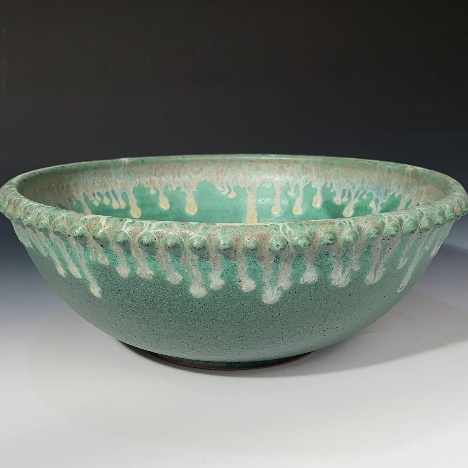 Side view of a large Juniper bowl in jade green with creamy drips and a row of beads along the rim.