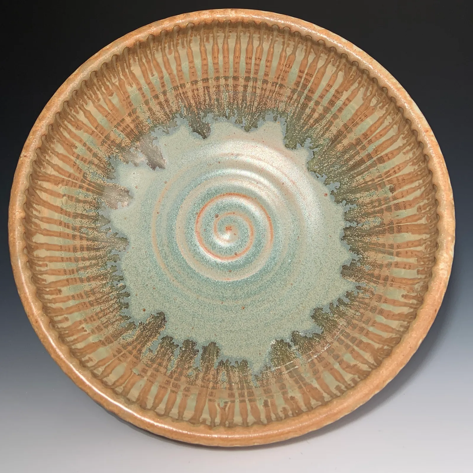 Willow bowl seen from above, with a jade green spiral at the center surrounded by carved ochre lines and drips.